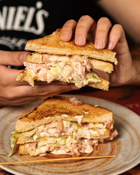 Club sandwich dello Shameless Pub tenuto in mano, con pollo, bacon e insalata